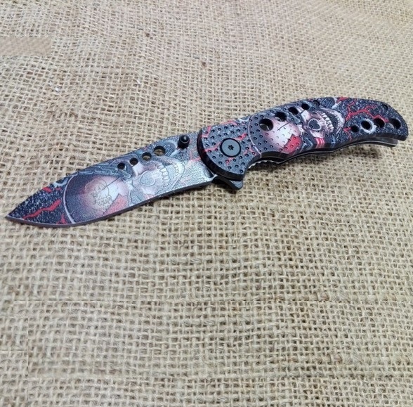 Coltello serramanico skull 03 - coltello a lama mobile interamente decorato con teschi imprigionati da catene e fulmini rossi .